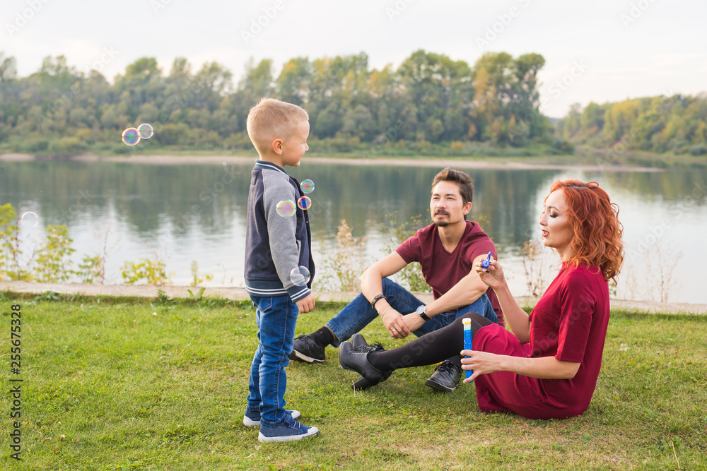 Family and nature concept - Mother, father and their child playing with colorful soap bubbles Family and nature concept - Mother, father and their child playing with colorful soap bubbles