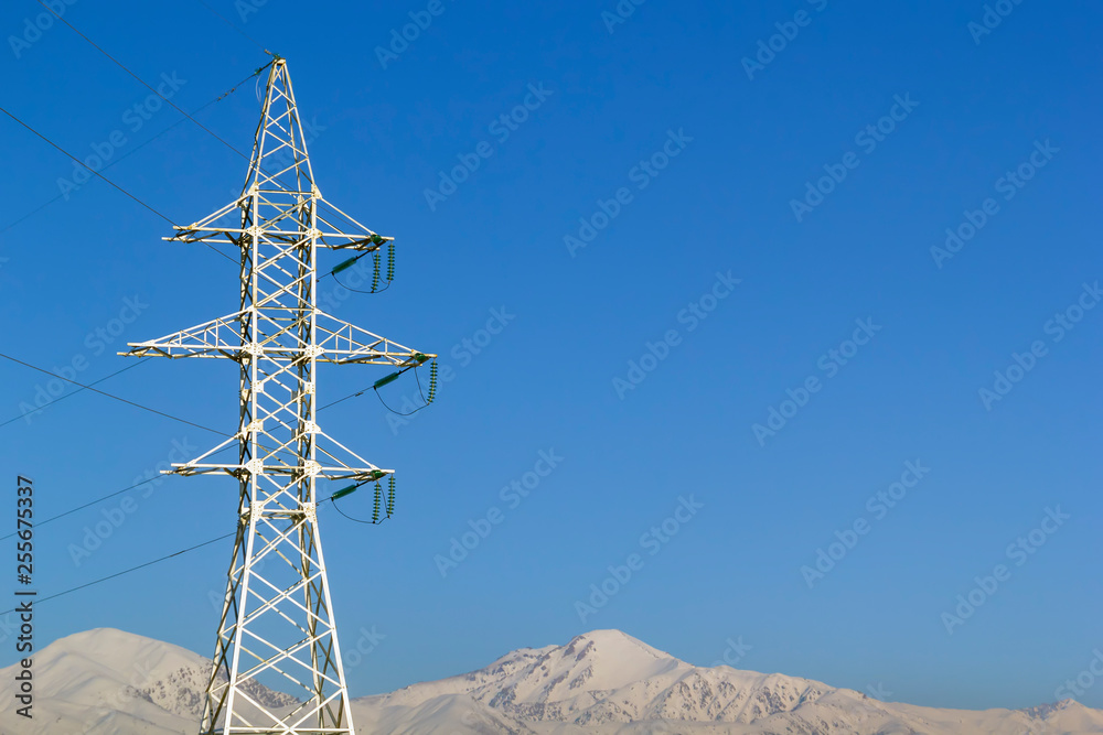 Electricity pole against the blue sky and snowy mountains. Copy space