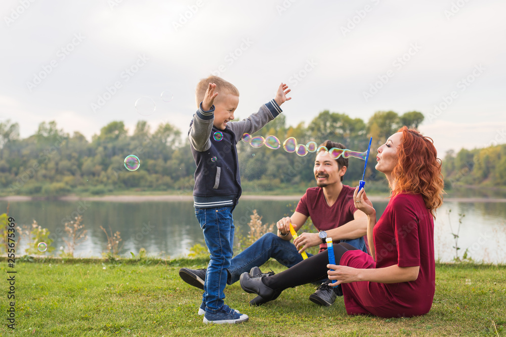 Family and nature concept - Mother, father and their child playing with colorful soap bubbles