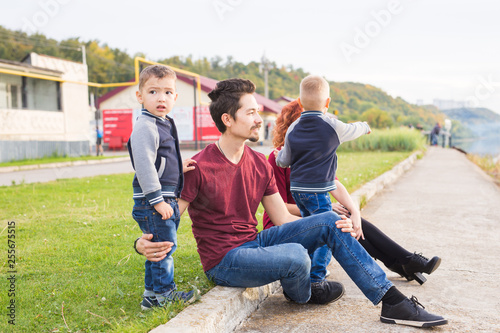 Parenthood, childhood and nature concept - Family sitting on the green ground and looking at small boat © satura_