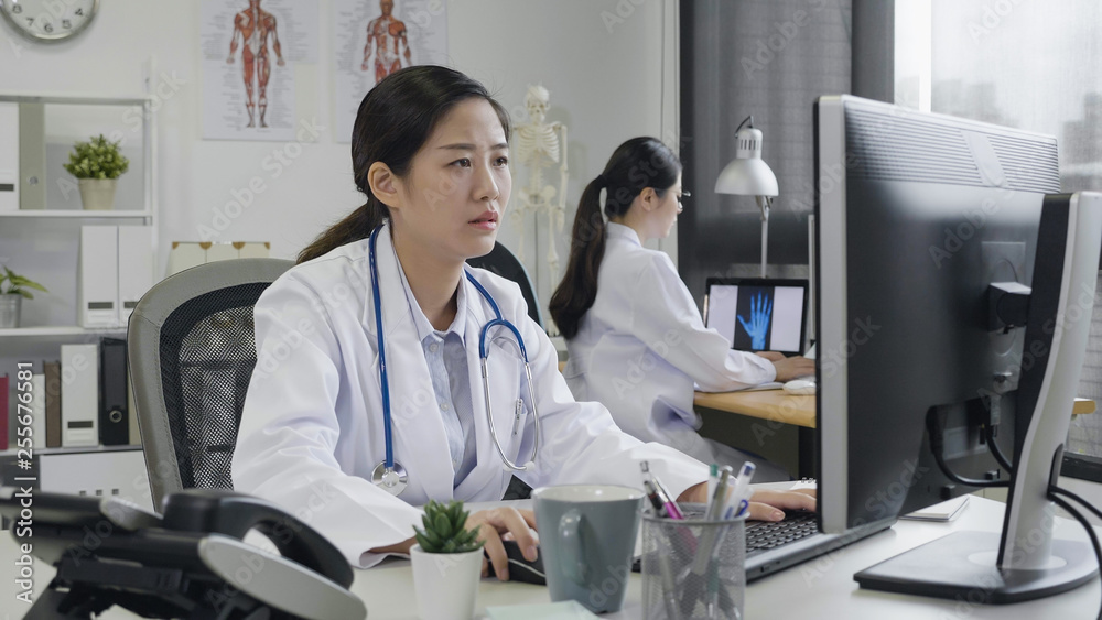 Obraz premium Female doctors in modern office working at computer in hospital. young asian woman medical staff sitting at desk in clinic concentrated typing on keyboard indoors. nurse with stethoscope health care