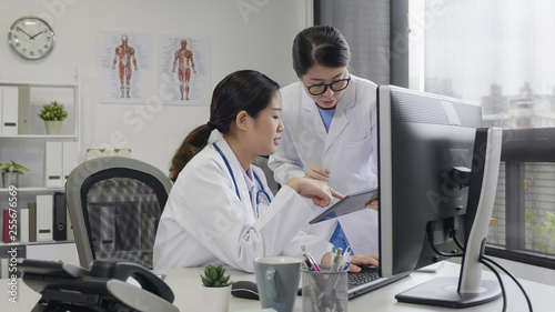 Confident asian woman doctors discussing about patient report on digital pad in office in hospital. female intern asking problem to experienced medical staff in clinic. coworkers talking conversation