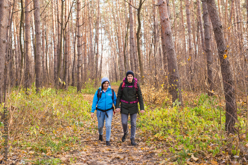 Travel, tourism, hike and people concept - Couple with backpacks walking in the autumn forest Travel, tourism, hike and people concept - Couple with backpacks walking in the autumn forest