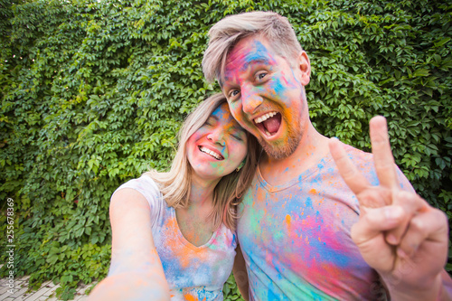 Holiday, holi and people concept - Woman and man with painted faces taking selfie over bush backgrund
