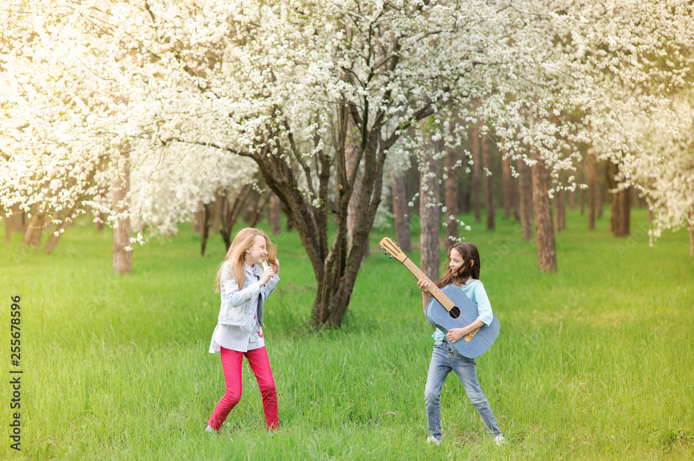 kids rock band of two funny little girls with vintage guitar and hairbrush as microphone playing music in spring blossom park outdoor