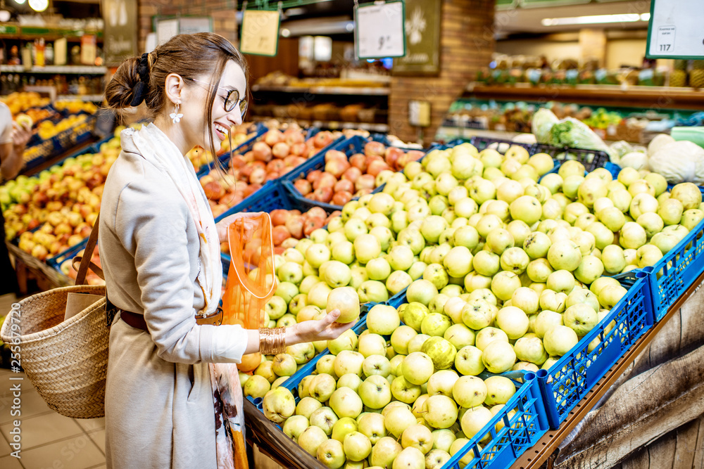 Young woman choosing apples to buy standing in the department with fruits and vegetables in the supermarket