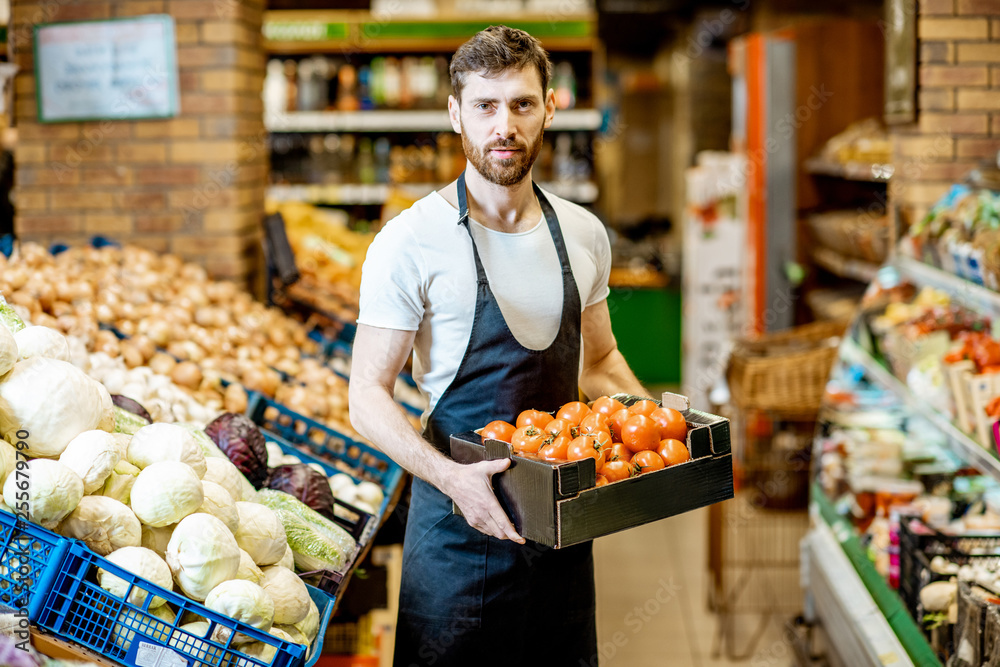 Portrait of a handsome shop worker or farmer holding box with fresh tomatoes in the vegetable department in the supermarket