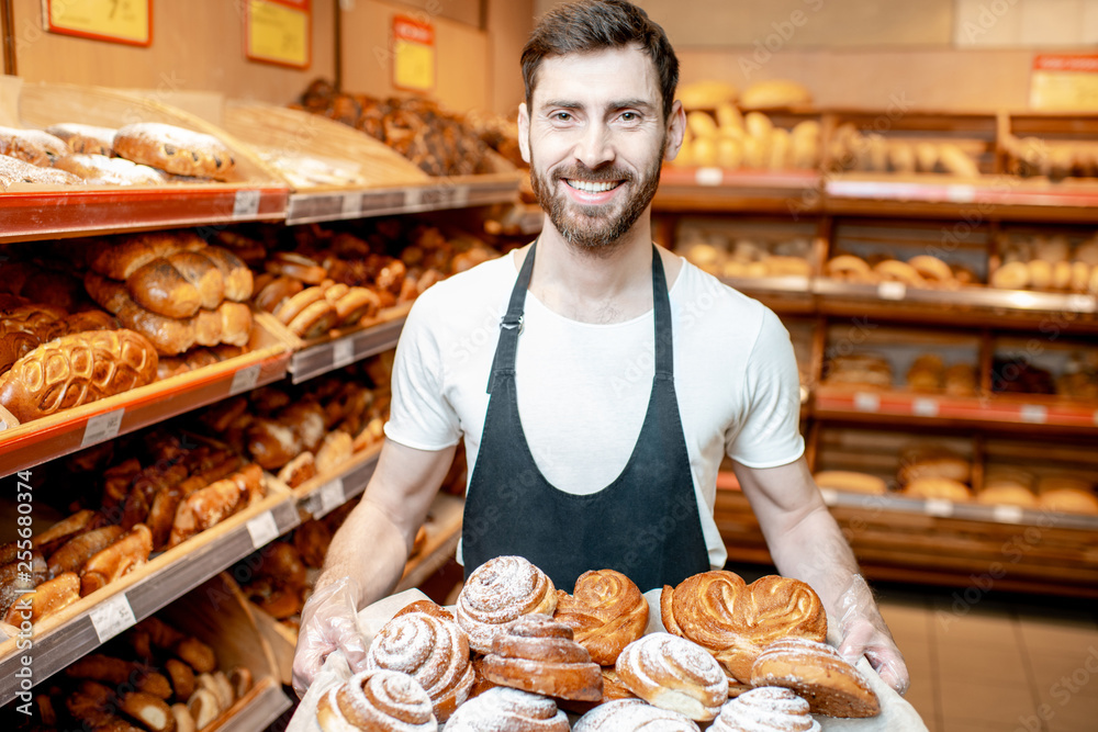 Portrait of a handsome baker in uniform standing with fresh pastries in the bakery deparment of the supermarket