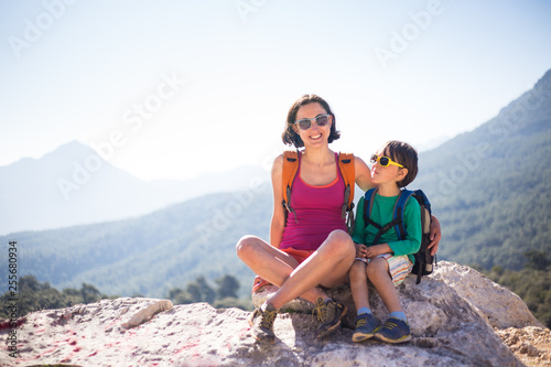 The boy and his mother are sitting on the top of the mountain.