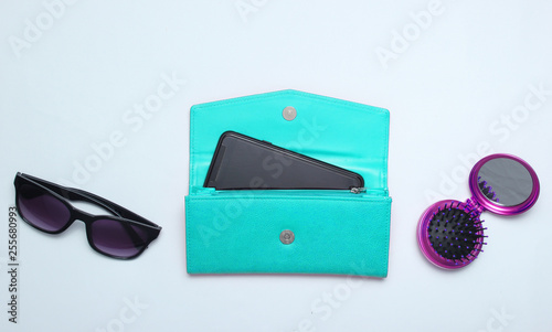 Smartphone in blue leather wallet, sunglasses, mirror hairbrush on a white background. Top view