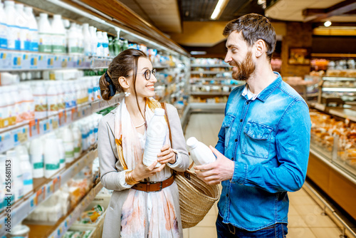 Young couple choosing milk standing together near the shelves with dairy products in the supermarket