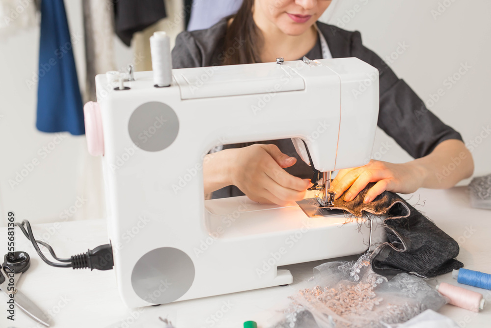 People and fashion concept - Young dressmaker woman sews clothes on sewing machine