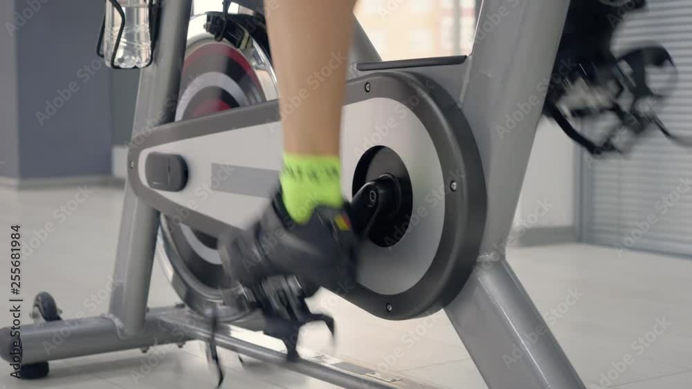 Woman legs spinning pedals on the spin bike. Seamless loop, woman spinning pedals on the static bike, Cycling workout concept. Close-up rotation pedal indoor bike cycling