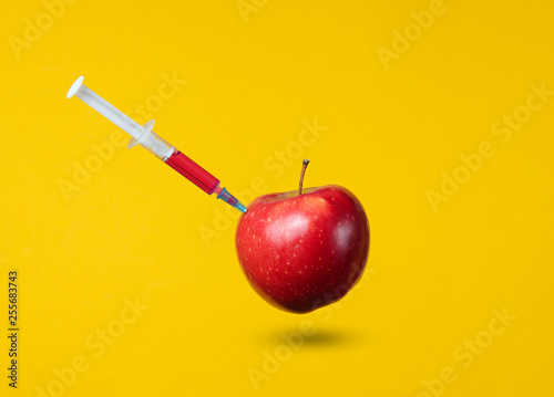Genetically modified Red Apple with syringes on yellow background. Medical Syringe injecting GMO in apple, fruit concept minimal