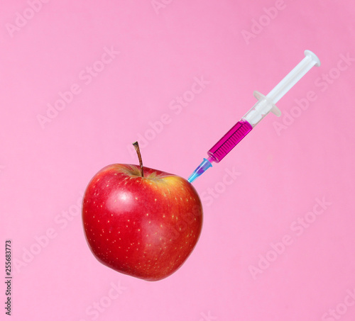 Genetically modified Red Apple with syringes on pink background.Medical Syringe injecting GMO in apple