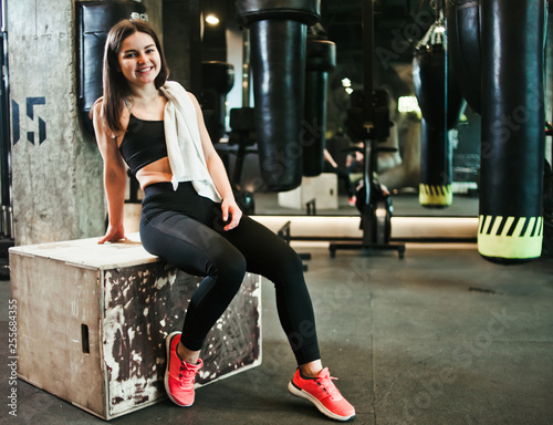 Break time. Smiling fit girl in sportswear sitting on a wooden box in the gym