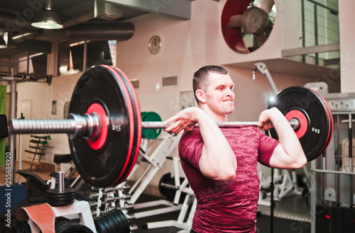 Power and strength. Athletic man in sportswear doing a barbell jerk on the chest in the gym