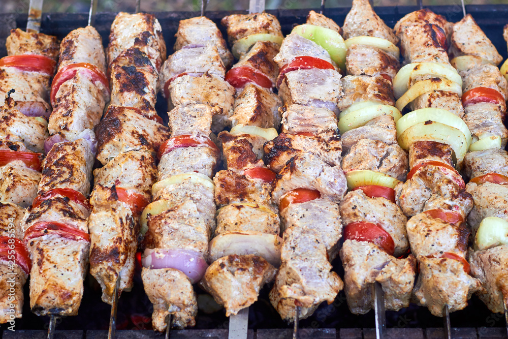 Pieces of juicy slices of marinated pork meat strung on skewers with slices of chopped tomatoes and onion preparing on barbecue grill over charcoal. Shashlik or Shish kebab popular in Eastern Europe.