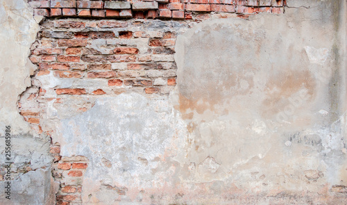 Old grungy red brick wall with peeled beige stucco background. Vintage retro plaster wall with dirty cracked scratched texture background