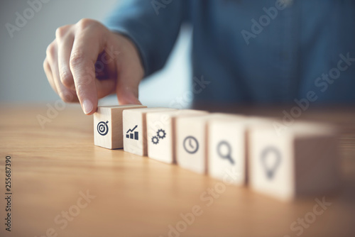 Woman hand arranging wood block with icon business strategy and Action plan.