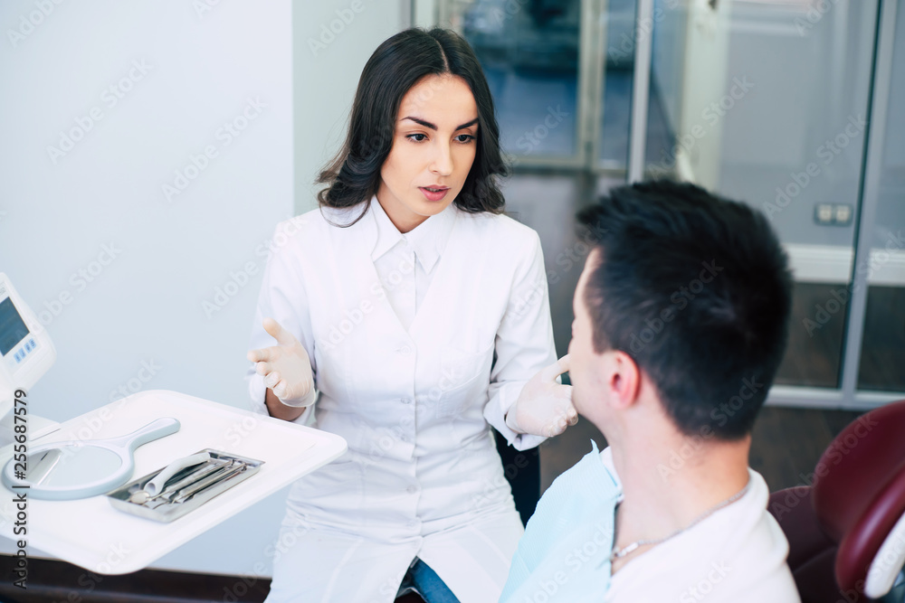 Fototapeta premium What are your complaints? A dentist on her work in the hospital is sitting right in front of a patient in medical clothes and asking about his complaints.