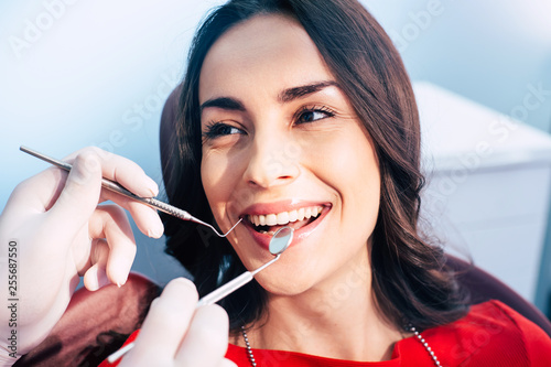 A girl with a brilliant white smile and healthy teeth  because of the doctor’s work is sitting in the dentist chair and enjoying the final result.