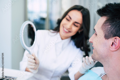 Dummy smile. A handsome patient of a beautiful dentist is smiling right into the mirror to estimate his new brilliant teeth.