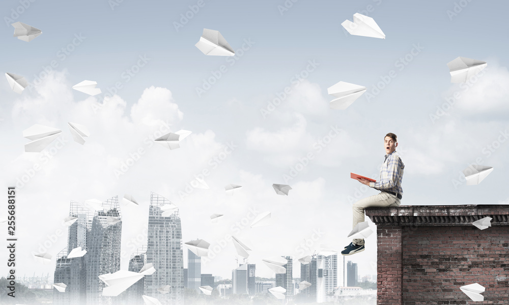 Handsome student guy on roof edge reading book and paper planes fly around Handsome student guy on roof edge reading book and paper planes fly around