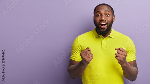 Photography Positive joyous glad young man keeps eyes widely opened, hands clenched in fists