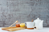 Ceramic teapot, white cup, honey in a glass jar and lemon on wooden background