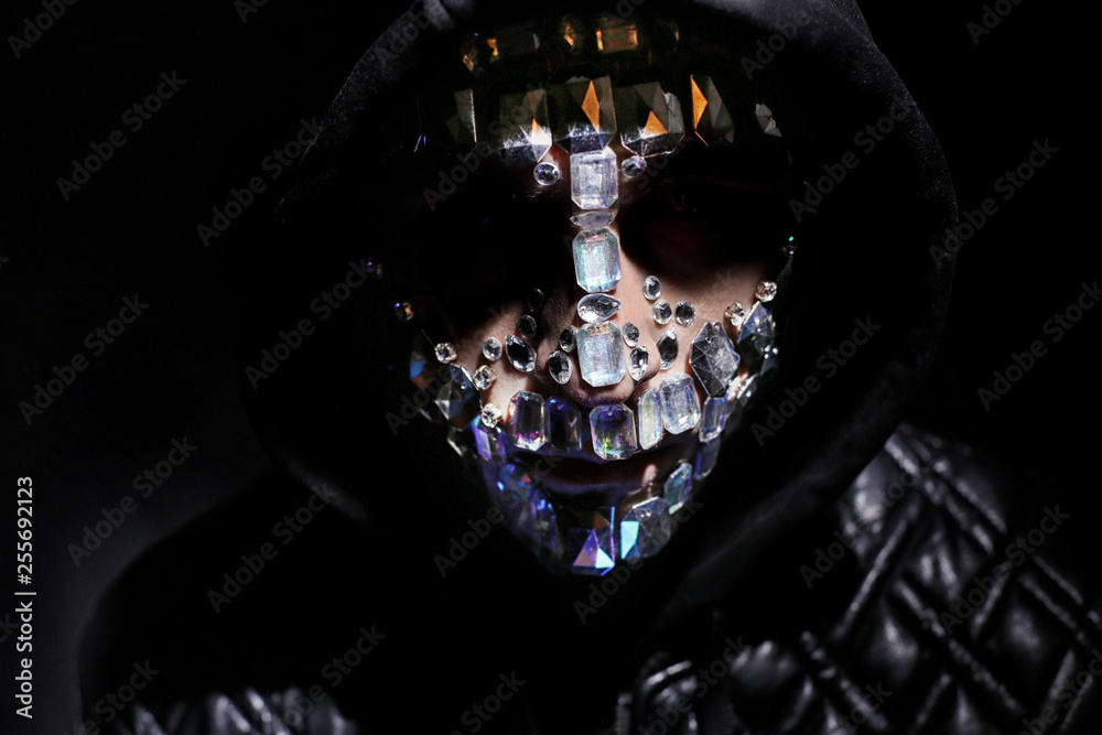 Art portrait of a hooded man with big rhinestones on his face. Mysterious  mystical appearance of