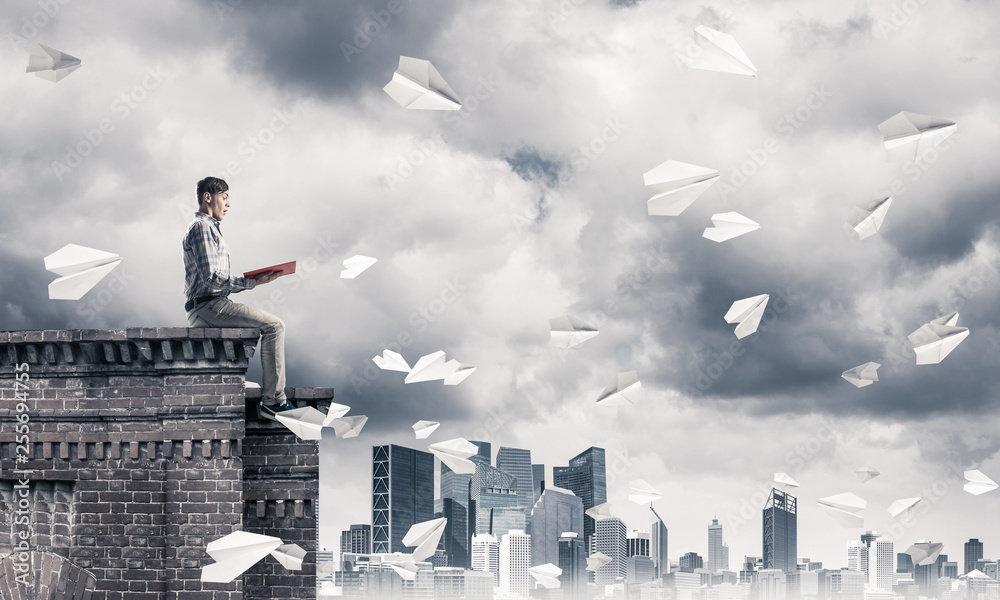Handsome student guy on roof edge reading book and paper planes Handsome student guy on roof edge reading book and paper planes