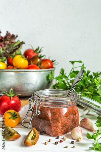 Food vegetables of different varieties of tomato and sauce in a glass jar on a white wooden table, handmade, preparation for preservation. Still life in a rustic style