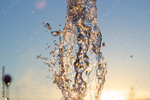 Сloseup jet of water from a fountain hit up against a blue sky, drops of water shimmer in the sun and the rays are reflected. Concept park outdoor recreation photo