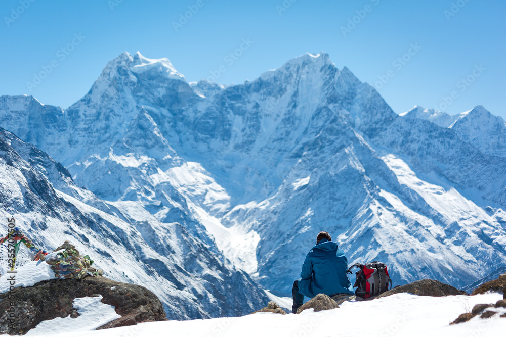 A man sits in the mountains on a hill and looks at the horizon. Think about life. Lying next to the backpack. Everest trekking. Himalayas. Nepal