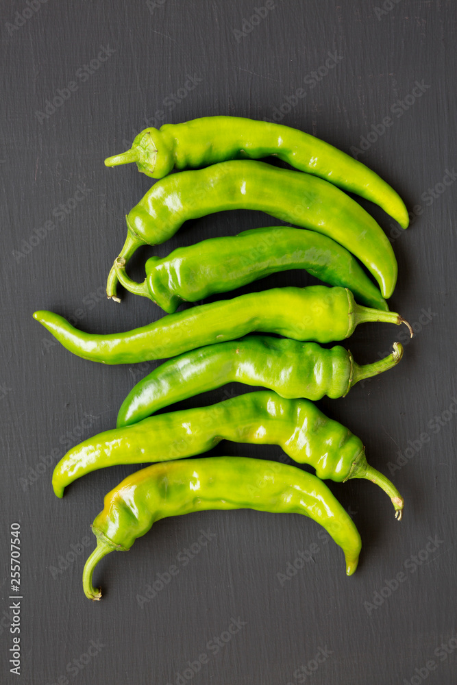 Green chili peppers on black surface, top view. Flat lay, from above, overhead. Close-up. Green chili peppers on black surface, top view. Flat lay, from above, overhead. Close-up.