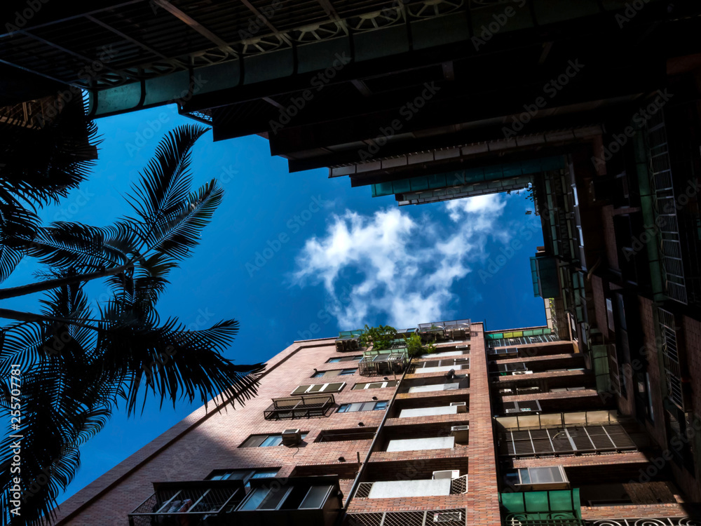 Looking up at the modern multistory apartment building against the cloudy sky. Skyward view of apartment building under bright blue cloudy sky. Apartment building from Low angle view. 