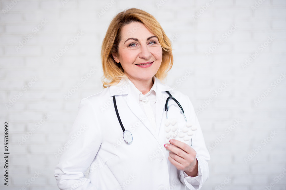 health care and pharmacy concept - mature female doctor or nurse holding pills over white wall