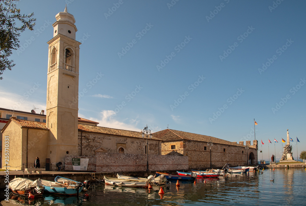 Scenic view of the Old Port of Lazise with the back of the Church of St Nicolò and docked boats, Veneto, Italy