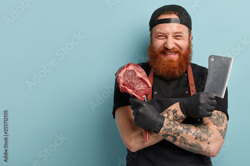 Industrial production concept. Satisfied butcher crosses hands over chest, hold necessary tool for cutting meat and piece of pork, works in large grocery store, takes out bones and trims off fat