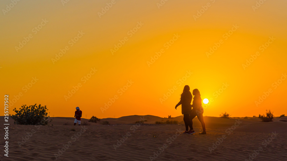 Couple at sunset over sand dunes in Dubai Desert Conservation Reserve, United Arab Emirates. Copy space for text.