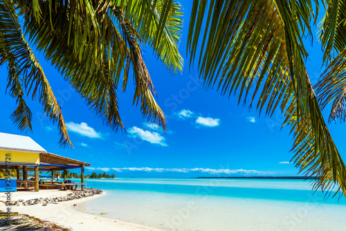 Stunning tropical Aitutaki island with palm trees, white sand, turquoise ocean water and blue sky at Cook Islands, South Pacific. With selective focus.