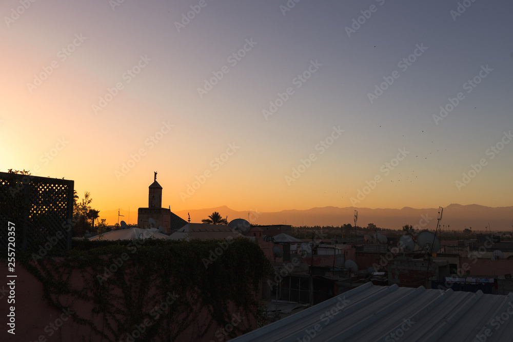 Sunrise / dawn over the roofs of Marrakesh with picturesque mosque and red glooming sky in front of the Atlas mountains (Marrakesh, Morocco, Africa)