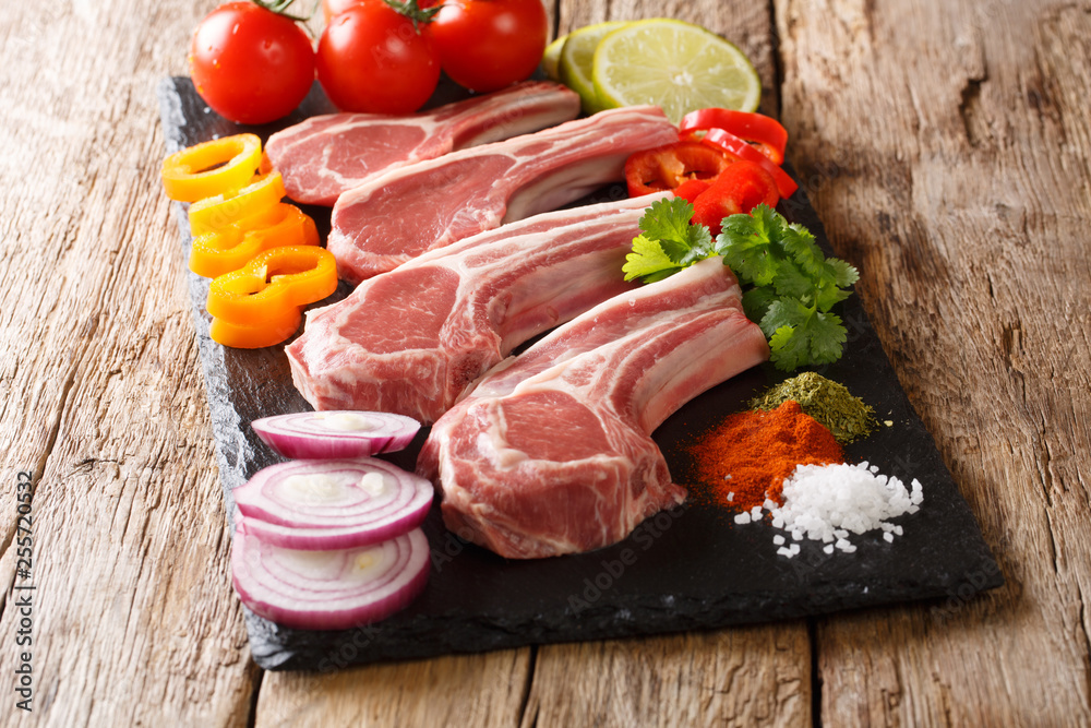 set of raw foods for cooking lamb cutlets with fresh vegetables and spices close-up on a slate board on the table. horizontal