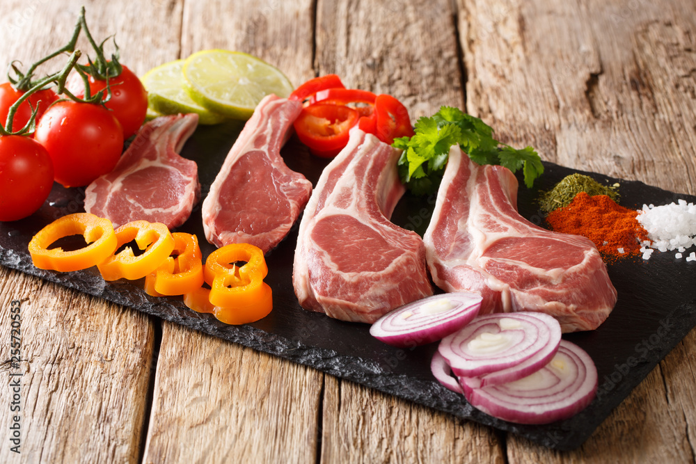 Preparation for grilling raw Lamb chops with fresh vegetables and spices close-up on a slate board. horizontal