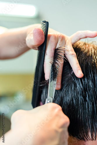 Close up of hairstylist's hands cutting strand of man's hair. Professional hairdresser or barber occupation. Male grooming concept.