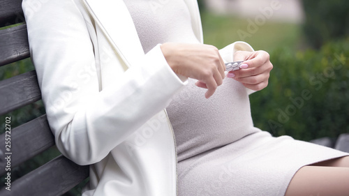 Pregnant female taking pill sitting on bench in park  prenatal care  medication