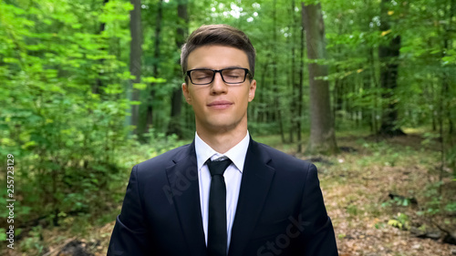Business person with closed eyes breathing deeply in forest, air freshener