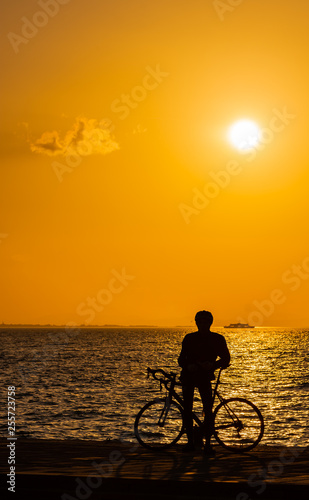 Silhouette of cyclist at sunset, orange sky and cloud