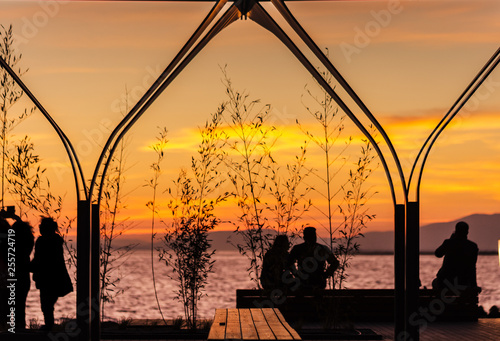 Silhouettes of people at sunset. Mountains and orange sky in the background. ...